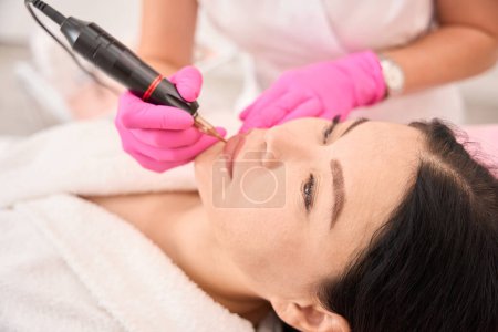 Photo for Decorative tattoo artist applies permanent lip makeup to a client using a special apparatus - Royalty Free Image