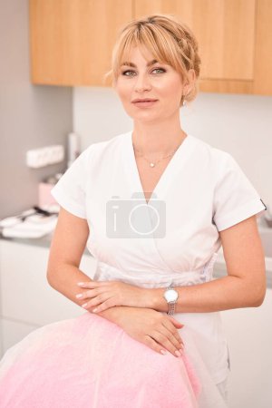 Téléchargez les photos : Belle femme blonde sur son lieu de travail dans une clinique de cosmétologie, elle est en uniforme soigné - en image libre de droit