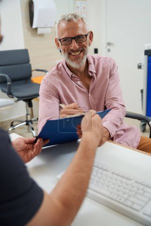 Téléchargez les photos : Homme âgé barbu signant des documents dans le bureau des médecins, les hommes assis au bureau - en image libre de droit