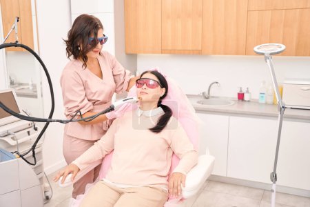 Téléchargez les photos : Femme subissant une procédure d'épilation faciale au laser dans une clinique de cosmétologie, le salon a un intérieur agréable - en image libre de droit