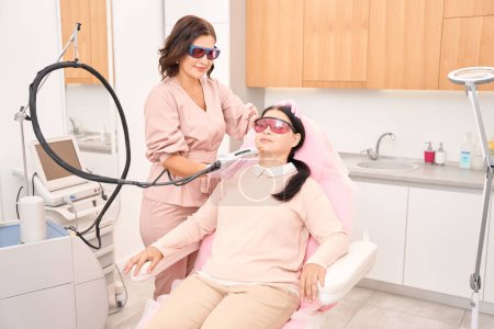 Foto de Cliente de una clínica de cosmetología se somete a un procedimiento de depilación facial con láser, el salón tiene un interior agradable - Imagen libre de derechos