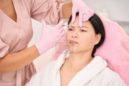 Foto de Moderno procedimiento de rejuvenecimiento por inyección en un salón de cosmetología, un especialista trabaja en guantes protectores rosados - Imagen libre de derechos