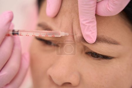 Foto de Procedimiento de rejuvenecimiento por inyección en un salón de cosmetología, un especialista trabaja en guantes protectores rosados - Imagen libre de derechos