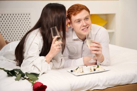 Téléchargez les photos : Couple heureux profitant d'un moment romantique avec champagne et dessert dans une chambre confortable - en image libre de droit