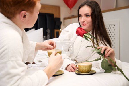 Téléchargez les photos : Couple romantique au lit avec tasses à café et rose rouge dans un cadre confortable chambre - en image libre de droit