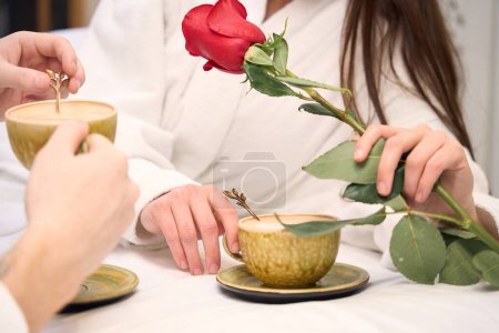 Téléchargez les photos : Vue rapprochée du couple dégustant un petit déjeuner romantique avec café et rose au lit - en image libre de droit