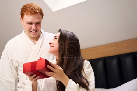 Téléchargez les photos : Jolie femelle en robe blanche recevant un cadeau de son petit ami dans un appartement contemporain - en image libre de droit