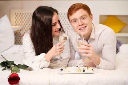 Téléchargez les photos : Couple heureux profitant d'un moment romantique avec champagne et dessert dans une chambre confortable - en image libre de droit