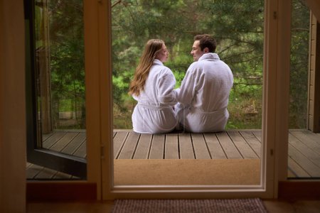 Téléchargez les photos : Couple mignon assis à l'entrée de la maison et se regardant respirer l'air frais de la forêt - en image libre de droit