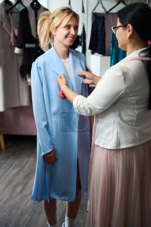 Téléchargez les photos : Femme souriante ayant un essayage dans un atelier de couture, le maître utilise des gadgets à coudre - en image libre de droit