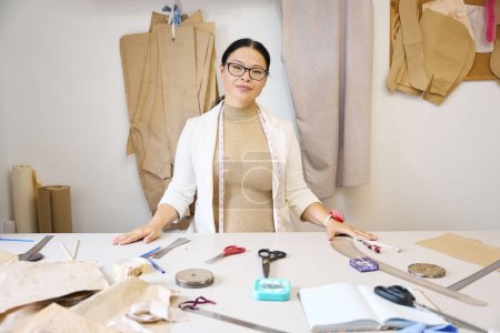 Foto de Hermosa mujer diseñadora en el taller en el lugar de trabajo, cosiendo gadgets en la mesa de corte - Imagen libre de derechos