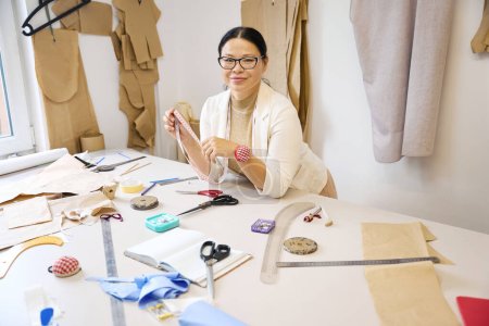 Foto de Lady diseñadora en el taller en el lugar de trabajo, recortando tela azul en la mesa de corte - Imagen libre de derechos