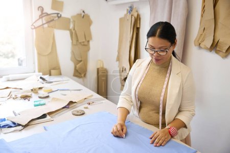 Foto de Lady diseñadora trabaja con tela azul en la mesa de cortar, la mujer usa tiza - Imagen libre de derechos