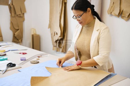 Téléchargez les photos : Dressmaker sur une table de découpe trace des motifs à la craie, un artisan travaille avec du tissu bleu - en image libre de droit