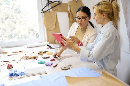 Foto de Las señoras diseñadores de moda utilizan la tableta en el lugar de trabajo, las mujeres están en la mesa de corte - Imagen libre de derechos