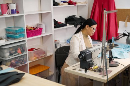 Téléchargez les photos : Femme sur le lieu de travail travaillant avec un tissu bleu, équipement moderne dans l'atelier - en image libre de droit