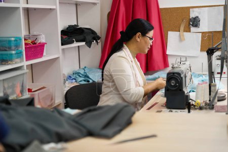 Téléchargez les photos : Femme en lunettes sur le lieu de travail travaille avec un chiffon bleu, dans l'atelier, il y a un équipement moderne - en image libre de droit