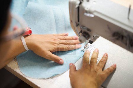 Téléchargez les photos : Dressmaker coud une robe sur une machine à coudre, le lieu de travail est bien éclairé - en image libre de droit