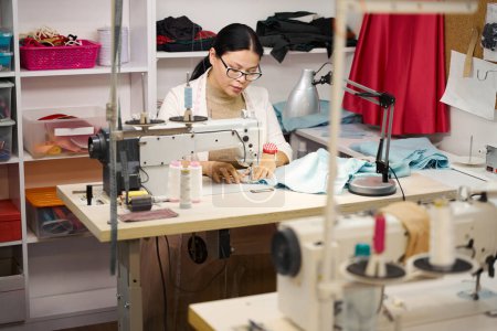 Photo for Woman sews on a sewing machine, there is good lighting in the room - Royalty Free Image