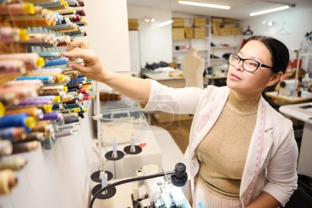 Téléchargez les photos : Femme sélectionne une bobine de fil sur un stand spécial, dans un atelier avec un équipement moderne - en image libre de droit