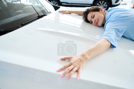 Foto de Mujer bonita con hermosa manicura que abraza la capucha del automóvil en la concesionaria de automóviles - Imagen libre de derechos