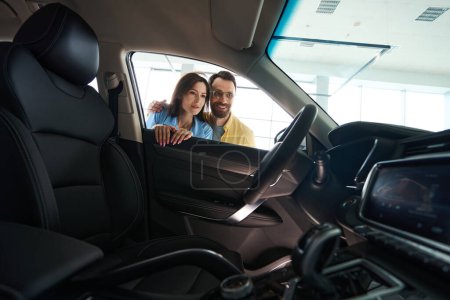 Foto de Hombre sonriente en gafas y mujer atractiva con hermosa manicura mirando el interior de auto en sala de exposición de coches - Imagen libre de derechos