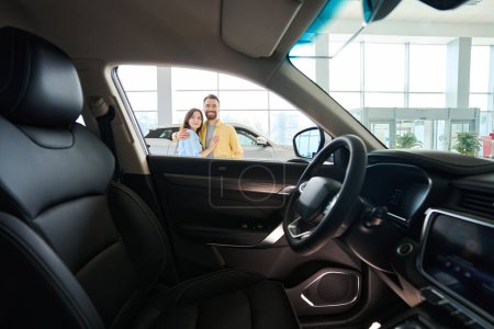 Foto de Foto de interior del coche con pareja amorosa posando en la cámara en el fondo en la sala de exposición del coche - Imagen libre de derechos