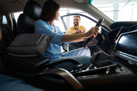 Foto de Atractiva hembra sentada en el interior del coche y sosteniendo el volante mientras su novio la mira en el centro del coche - Imagen libre de derechos