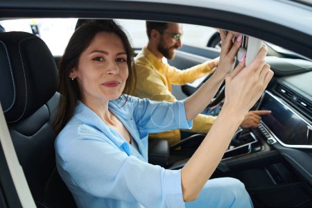 Photo for Young female looking at camera while sitting in car with her boyfriend - Royalty Free Image