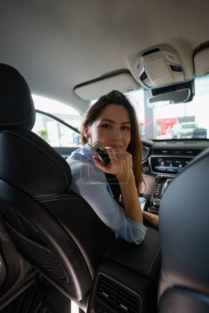 Foto de Mujer atractiva sosteniendo la llave del coche y mirando a la cámara mientras está sentado en el interior de automóviles - Imagen libre de derechos