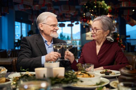 Foto de Alegre anciano hombre y mujer celebrando la Navidad juntos tintinear copas con champán en la cafetería - Imagen libre de derechos