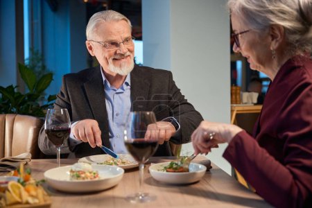 Photo for Smiling aged man and woman eating festive dinner in restaurant during New Year celebration - Royalty Free Image