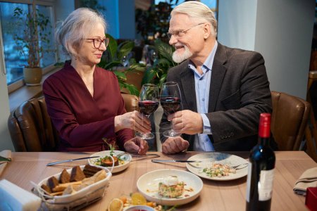 Photo for Aged woman and man enjoying festive dinner clinking wineglasses celebrating Christmas in cafe - Royalty Free Image