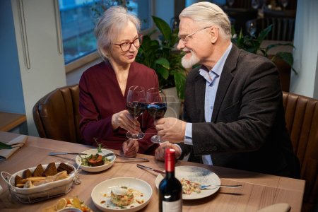 Foto de Mujer madura y hombre tintineo viñas celebrando la Navidad en el restaurante disfrutando de la cena de Año Nuevo - Imagen libre de derechos