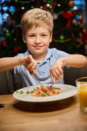 Photo for Cheerful little boy enjoying festive dinner during New Year celebrating in restaurant - Royalty Free Image
