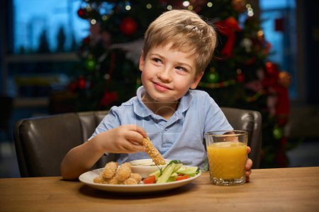 Photo for Dreamy cheerful little boy eating fast food in cafe on New Years Eve celebration - Royalty Free Image