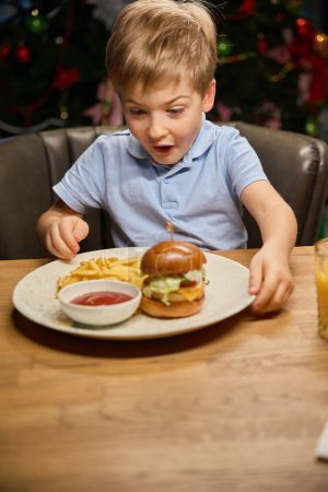 Foto de Sorprendido niño mirando su hamburguesa grande diciendo wow disfrutando de menú de comida rápida en la celebración de Año Nuevo - Imagen libre de derechos
