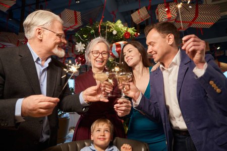 Photo for Happy laughing family with bright sparklers and glasses of champagne enjoying New Year night in restaurant - Royalty Free Image
