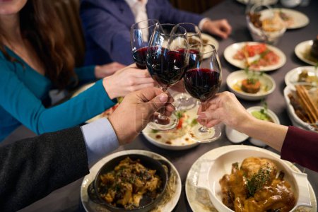 Téléchargez les photos : Les gens assis et cliquetis verres de vin à une table festive dans un restaurant - en image libre de droit