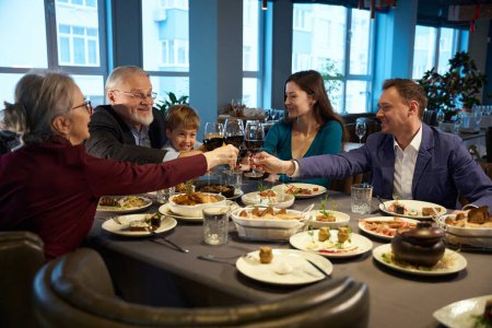 Foto de Familia feliz sosteniendo copas con vino mientras celebra la Navidad en el restaurante - Imagen libre de derechos