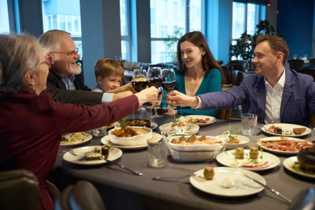 Photo for Smiling people clinking glasses of wine at a festive table in a restaurant, while celebrating Christmas - Royalty Free Image