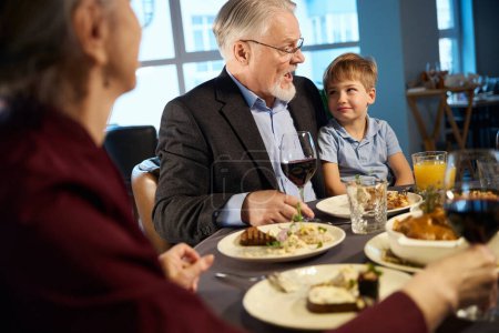 Téléchargez les photos : Vieil homme souriant et petit garçon assis à une table festive dans le restaurant, célébrant le Nouvel An - en image libre de droit