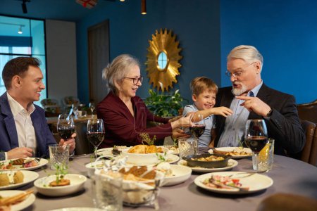 Photo for Aged man playing having fun with little boy while celebrating Christmas at dining table in restaurant - Royalty Free Image