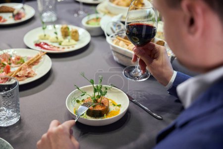 Foto de Hombre irreconocible sosteniendo copa de vino cenando en restaurante con sabrosos platos exóticos - Imagen libre de derechos