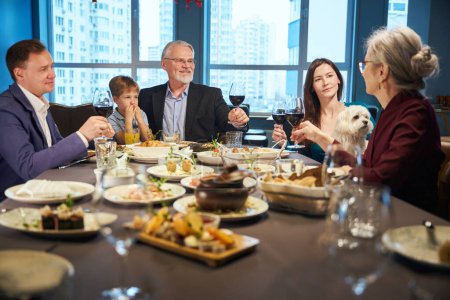 Téléchargez les photos : Famille profitant du dîner de Noël ensemble dans un restaurant confortable partageant des repas levant des verres avec toasting de vin célébrant vacances - en image libre de droit