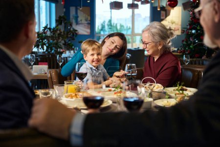 Foto de Joven alegre con niño sentado en el restaurante durante la celebración de Navidad disfrutando de la comunicación familiar - Imagen libre de derechos