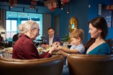 Téléchargez les photos : Heureuse femme âgée profitant d'un moment heureux avec un petit garçon tout en célébrant le Nouvel An au restaurant - en image libre de droit