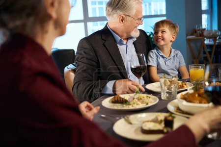 Téléchargez les photos : Vieil homme souriant et petit garçon se regardant dans le restaurant assis à la table - en image libre de droit