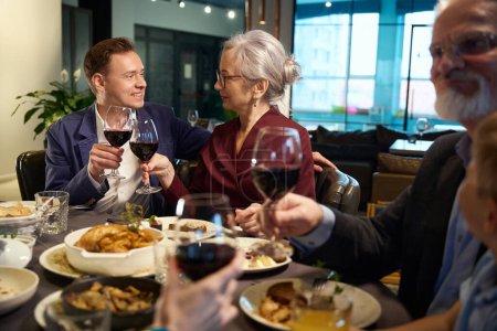 Foto de Hombre y mujer sonrientes brindando con copas con vino, celebrando las vacaciones de invierno en el restaurante - Imagen libre de derechos