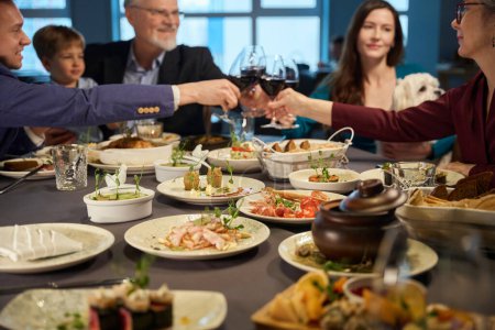 Téléchargez les photos : Famille savourant le réveillon du Nouvel An dîner ensemble dans un restaurant confortable boire du vin rouge pour trinquer et célébrer les vacances - en image libre de droit